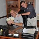 Men at a desk smiling and showing cash